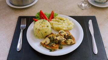 Une assiette de nourriture comprenant de la purée de pommes de terre, une salade verte et un plat de viande, le tout servi sur un set de table noir.