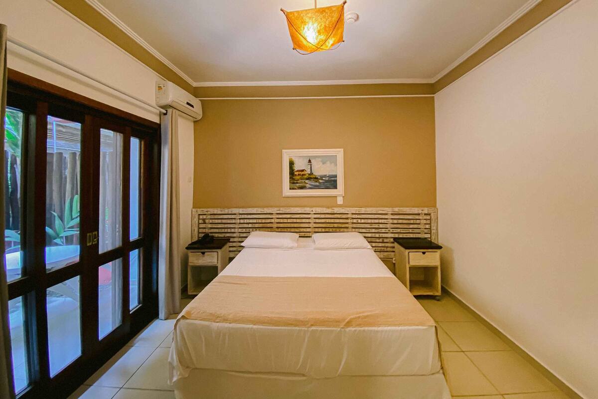 A hotel room with a bed, bedside tables, a painting on the wall, and a window with curtains.
