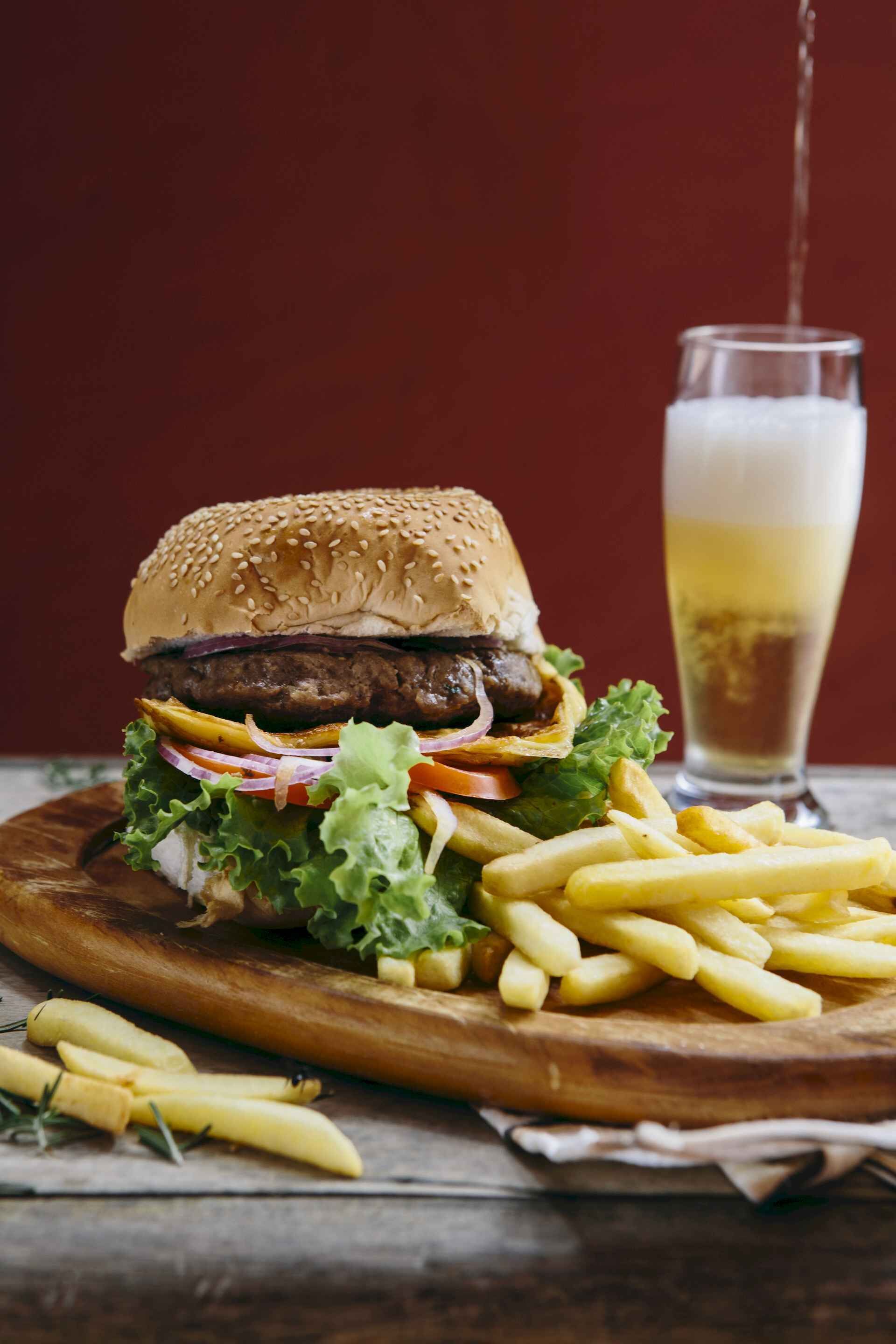 A burger with fries and a glass of beer on a wooden board.