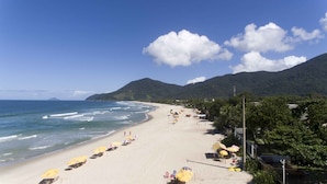 A beach with rows of yellow umbrellas and beach chairs, a sandy shore, and a mountain in the background. - Pousada Porto Mare (São Sebastião)
