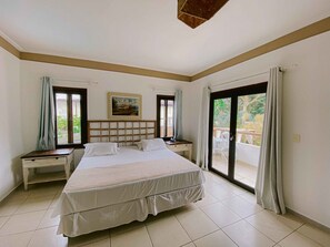 A bedroom with a large bed, two bedside tables, a painting on the wall, and a balcony with curtains. - Pousada Porto Mare (São Sebastião)