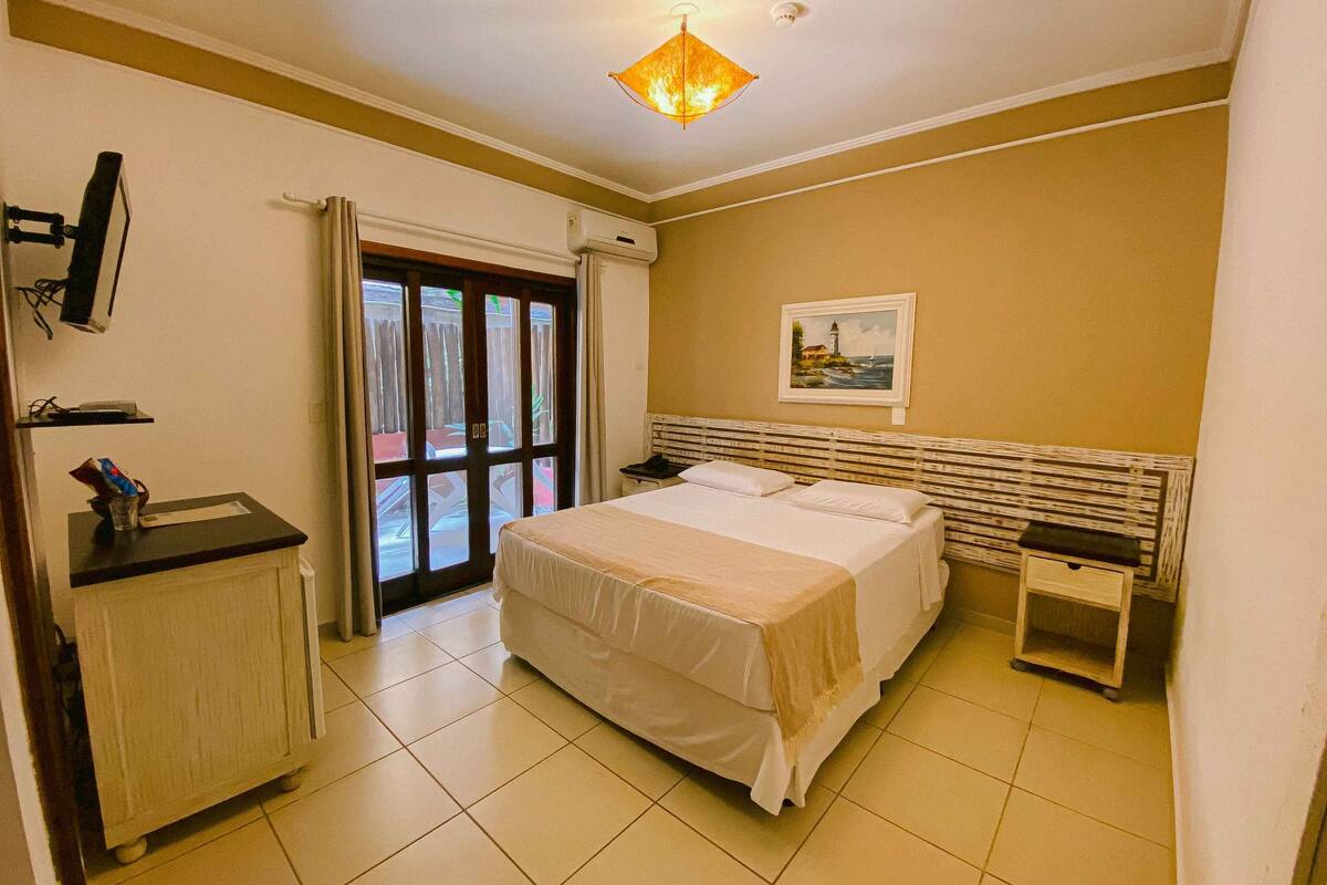 A hotel room with a bed, a desk, a chair, a TV, and a painting on the wall.