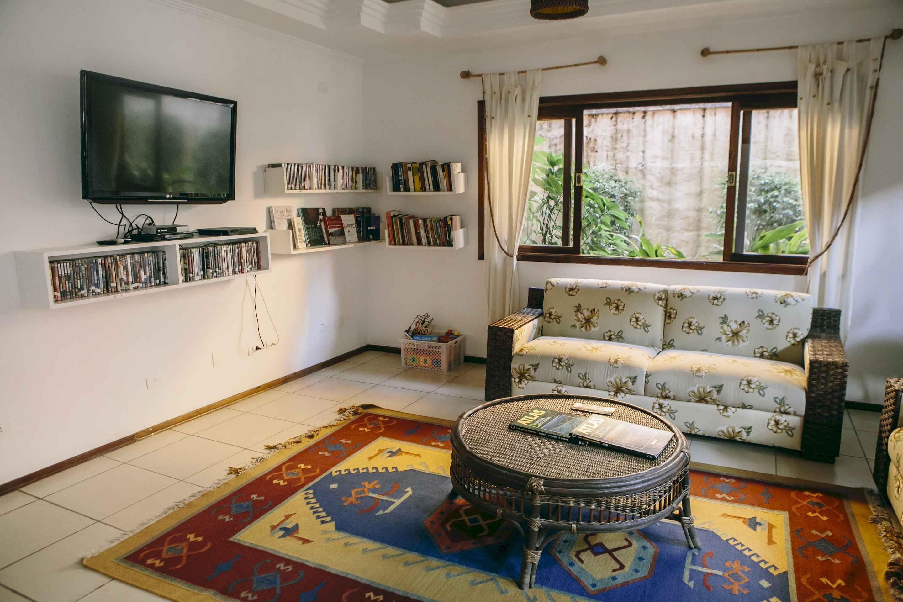 Uma sala de estar com televisão de tela plana, estantes, um sofá, uma mesa de centro redonda e um tapete estampado.
