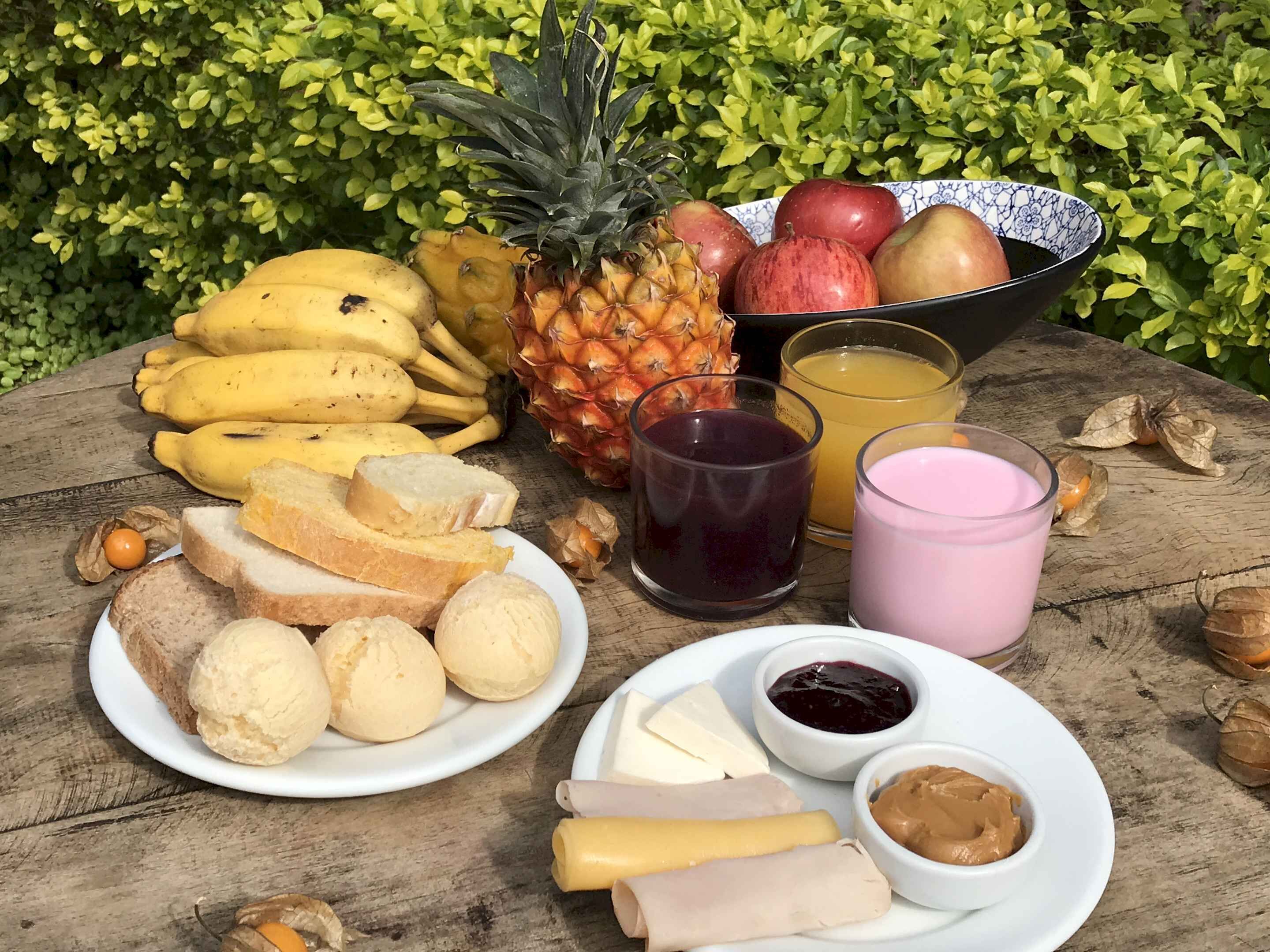 Una mesa de madera con una preparación para picnic que incluye frutas, pan, queso y condimentos.
