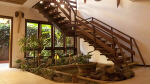 A wooden staircase with a view of tropical plants and a large window. - Pousada Porto Mare (São Sebastião)