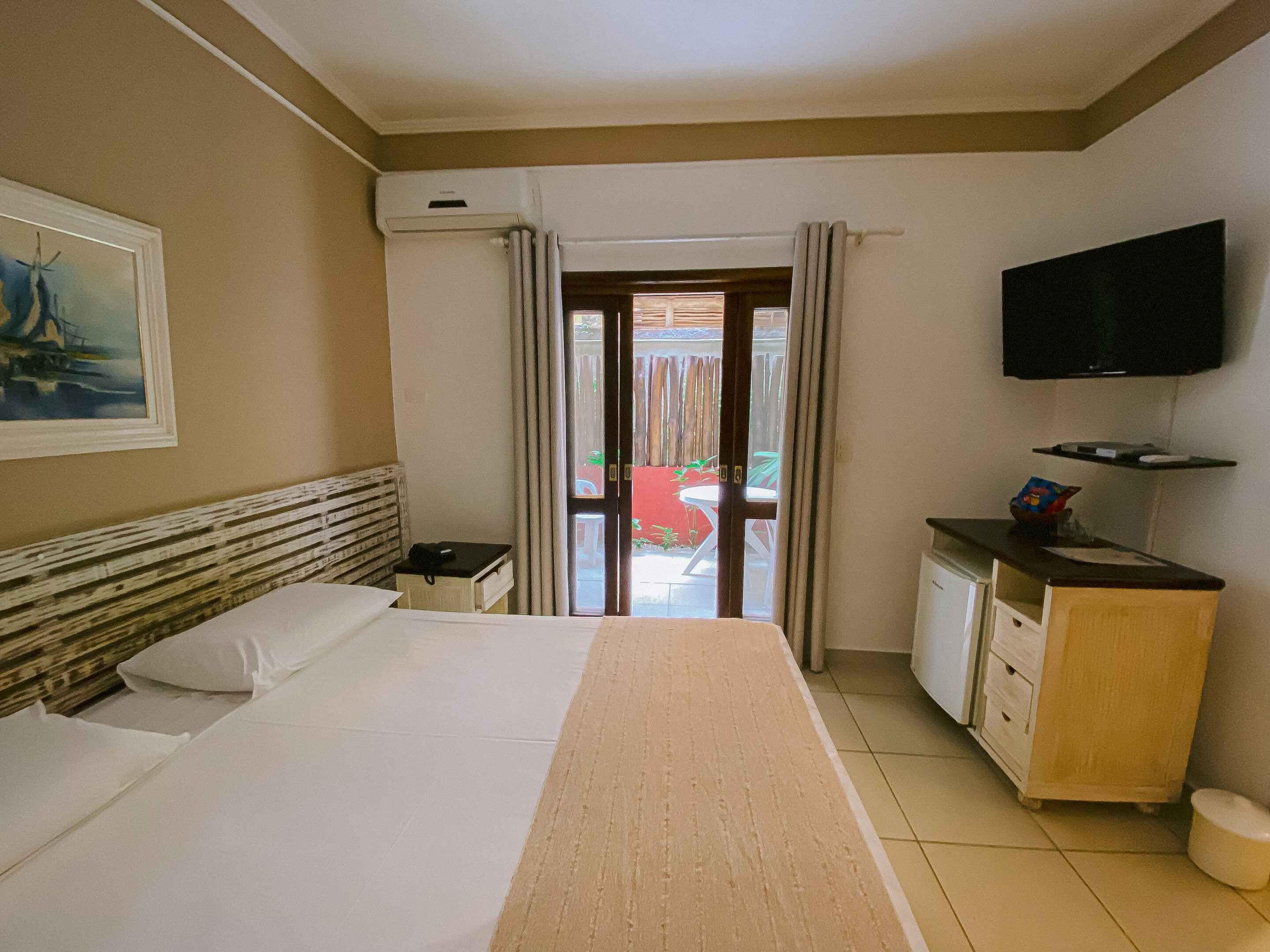 A hotel room with a bed, a desk with a chair, a television, and a view of the outside.