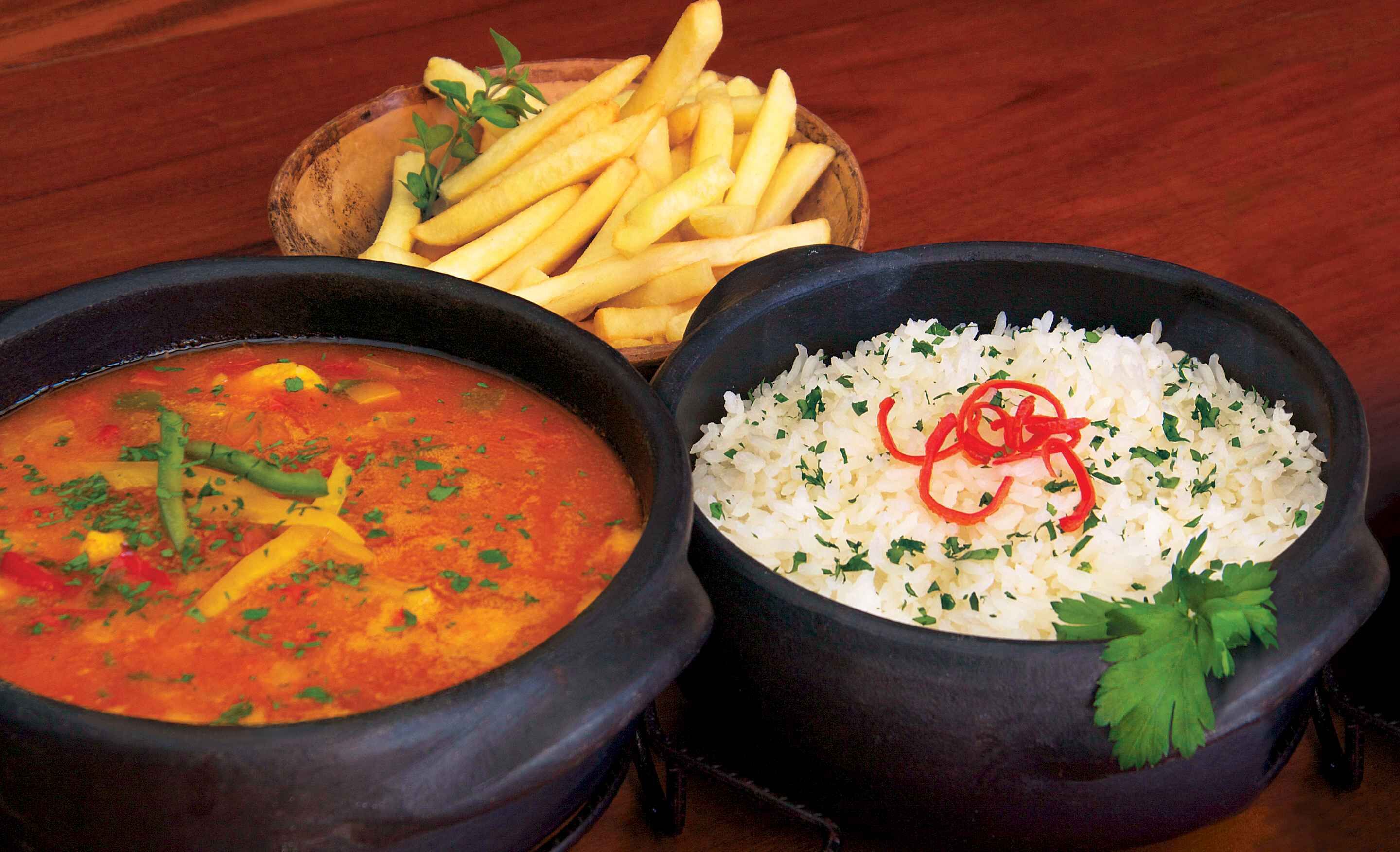 A meal consisting of a soup with vegetables, rice garnished with herbs, and French fries.