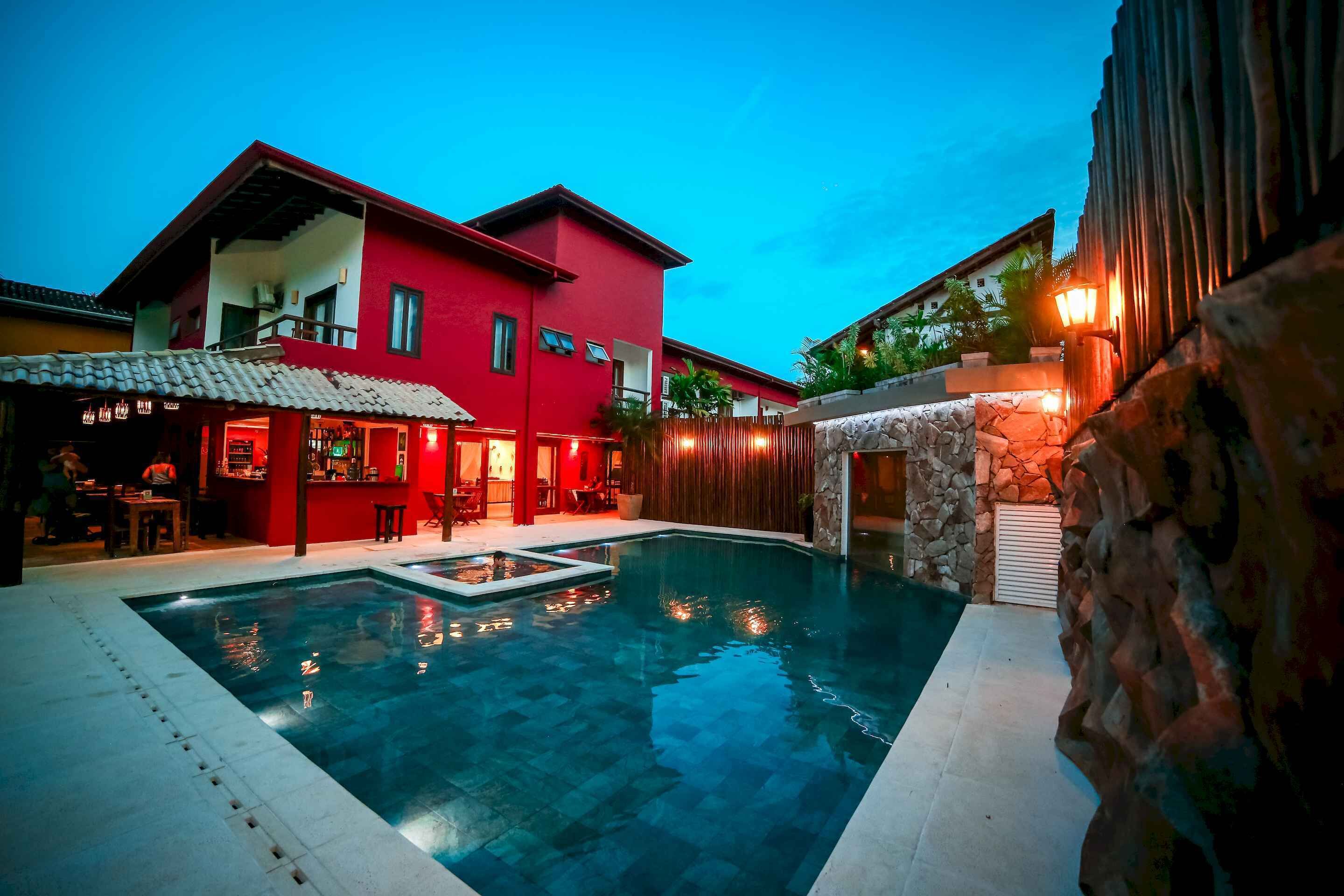 A swimming pool surrounded by a red building with a bar area and a stone wall.