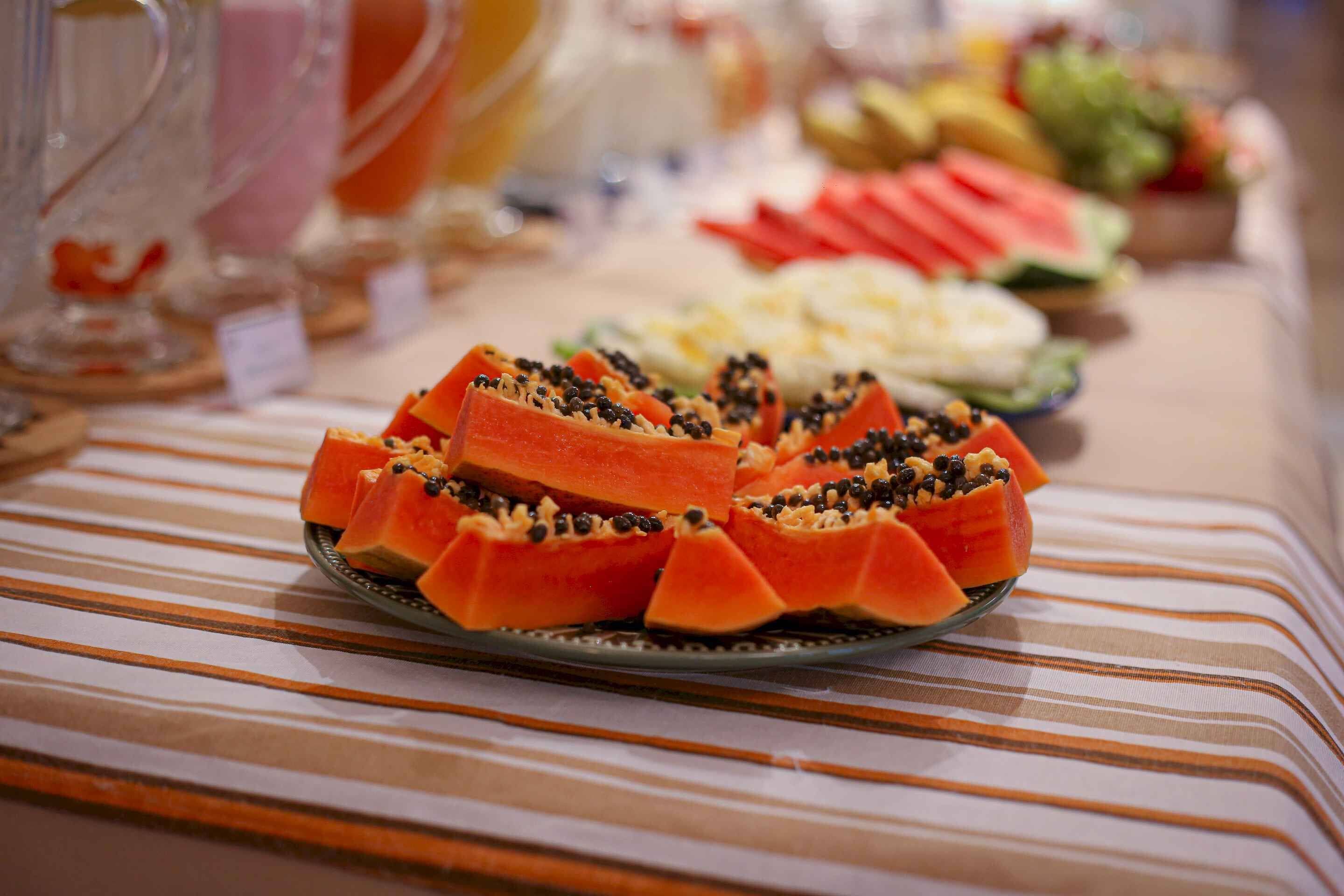 Una mesa de buffet con diversos platos, incluyendo un destacado despliegue de papaya en rodajas adornada con semillas negras.