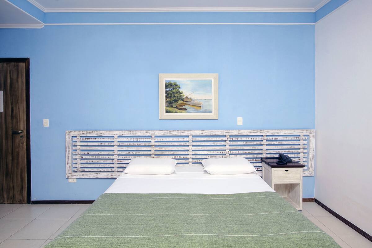 A room with a bed, a headboard with a patterned design, a painting on the wall, and a door.