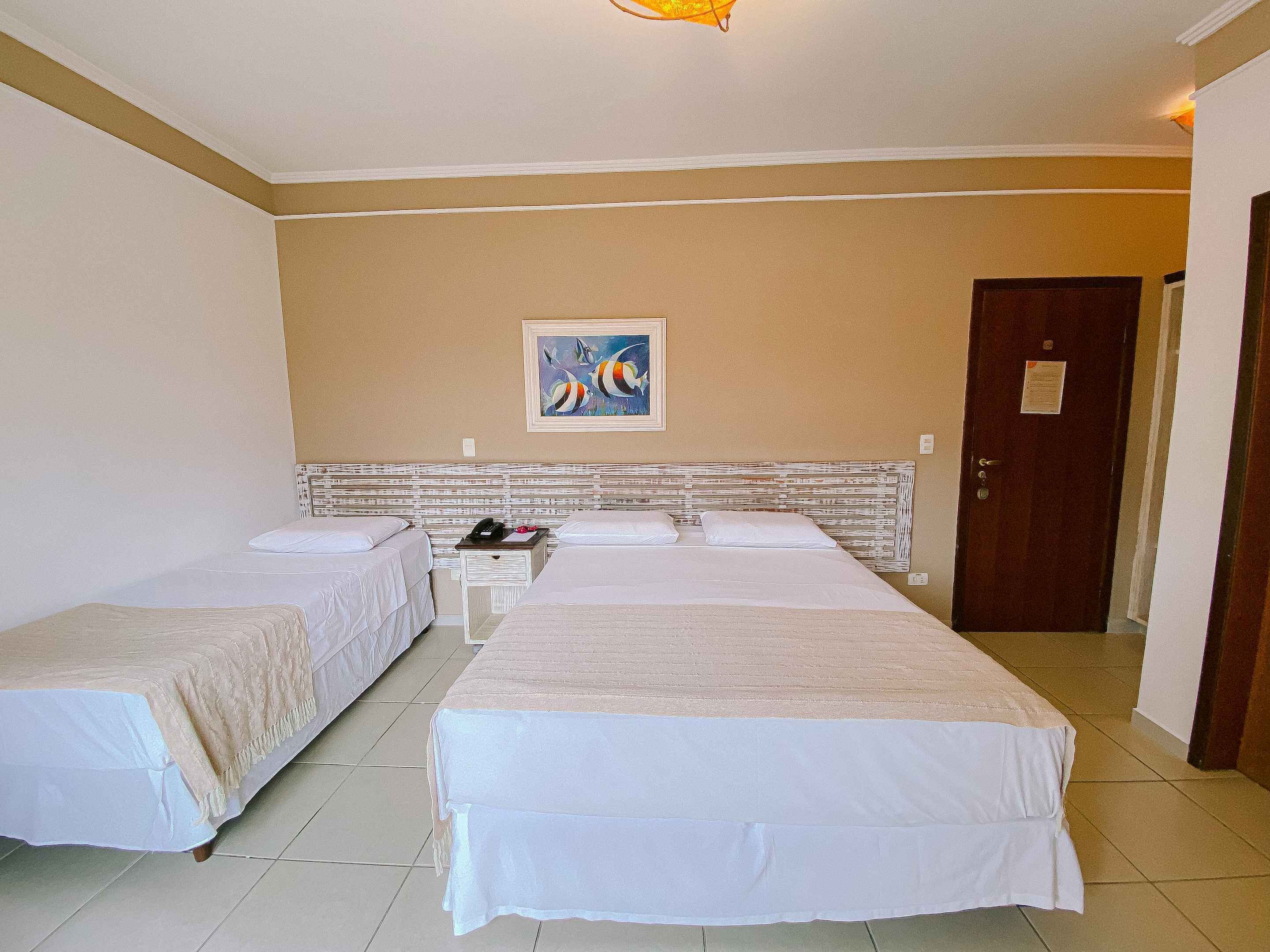 Habitación de hotel con dos camas, una mesita de noche, un cuadro en la pared y una puerta.