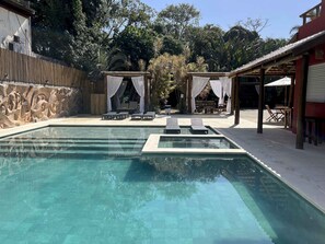 A swimming pool with lounge chairs, a covered seating area, and a stone wall. - Pousada Porto Mare (São Sebastião)