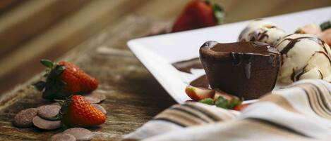 Un plato de postre con salsa de chocolate, fresas y helado sobre una mesa de madera.