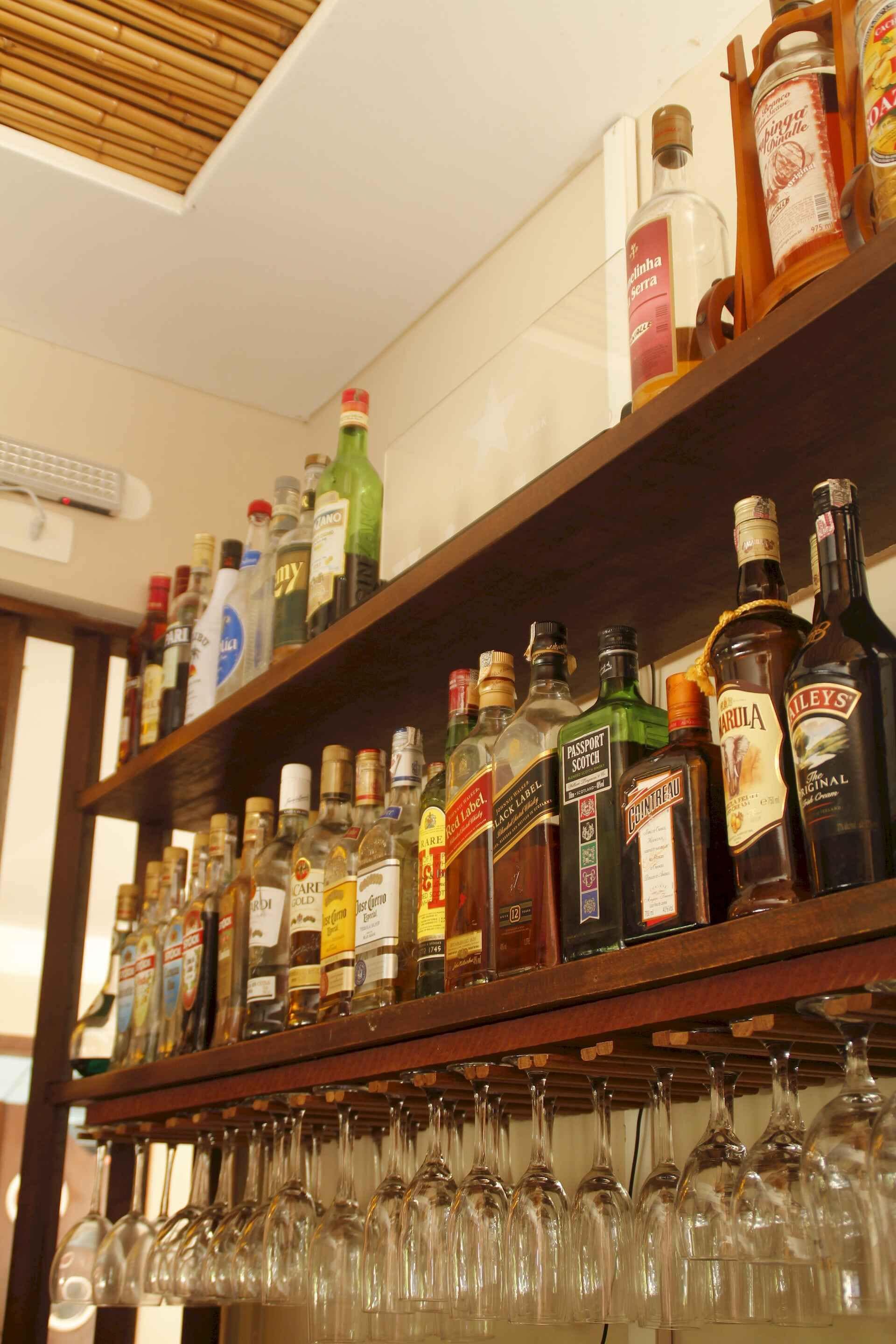 A bar area with shelves of liquor bottles and a row of empty wine glasses.