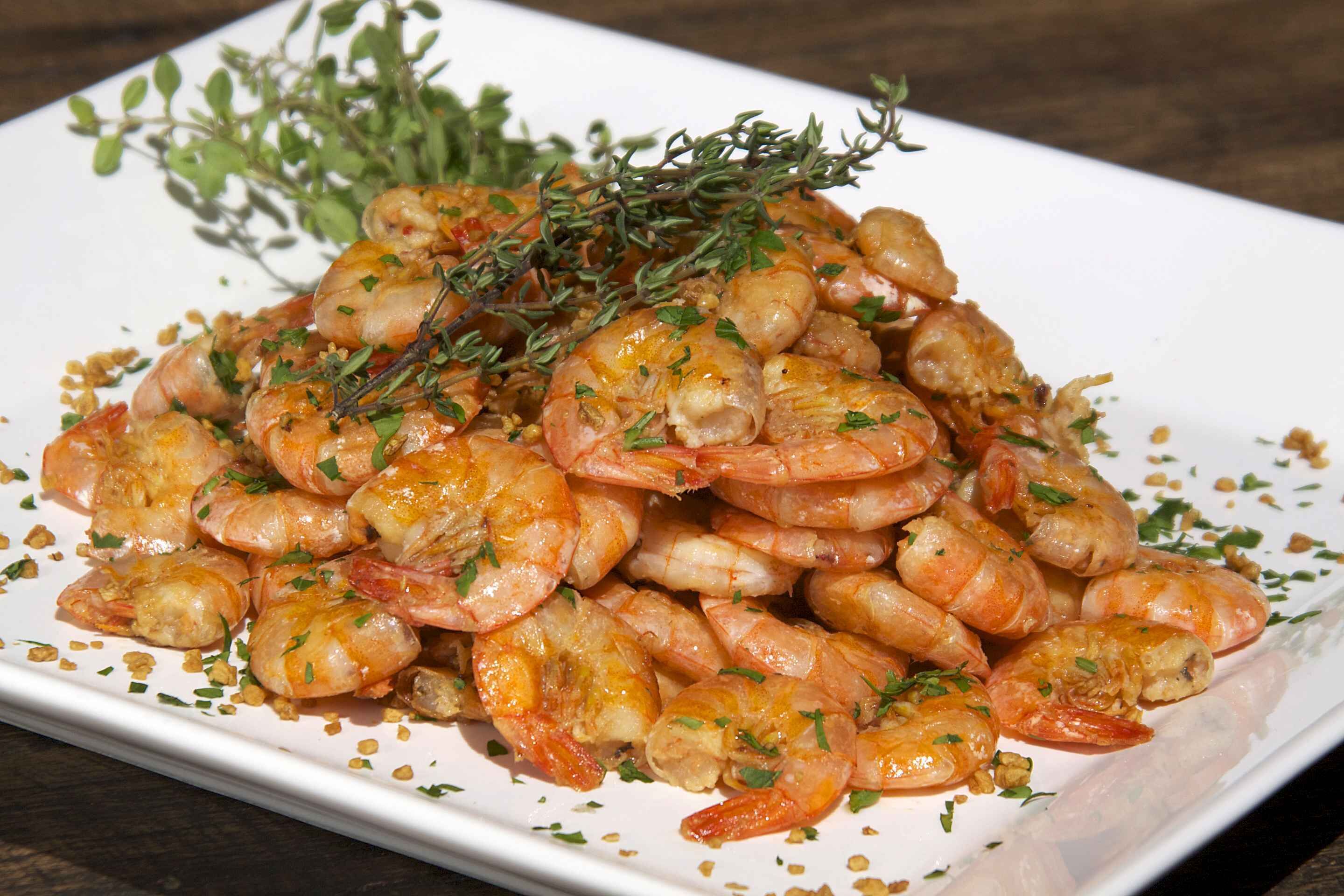 A plate of cooked shrimp garnished with herbs.