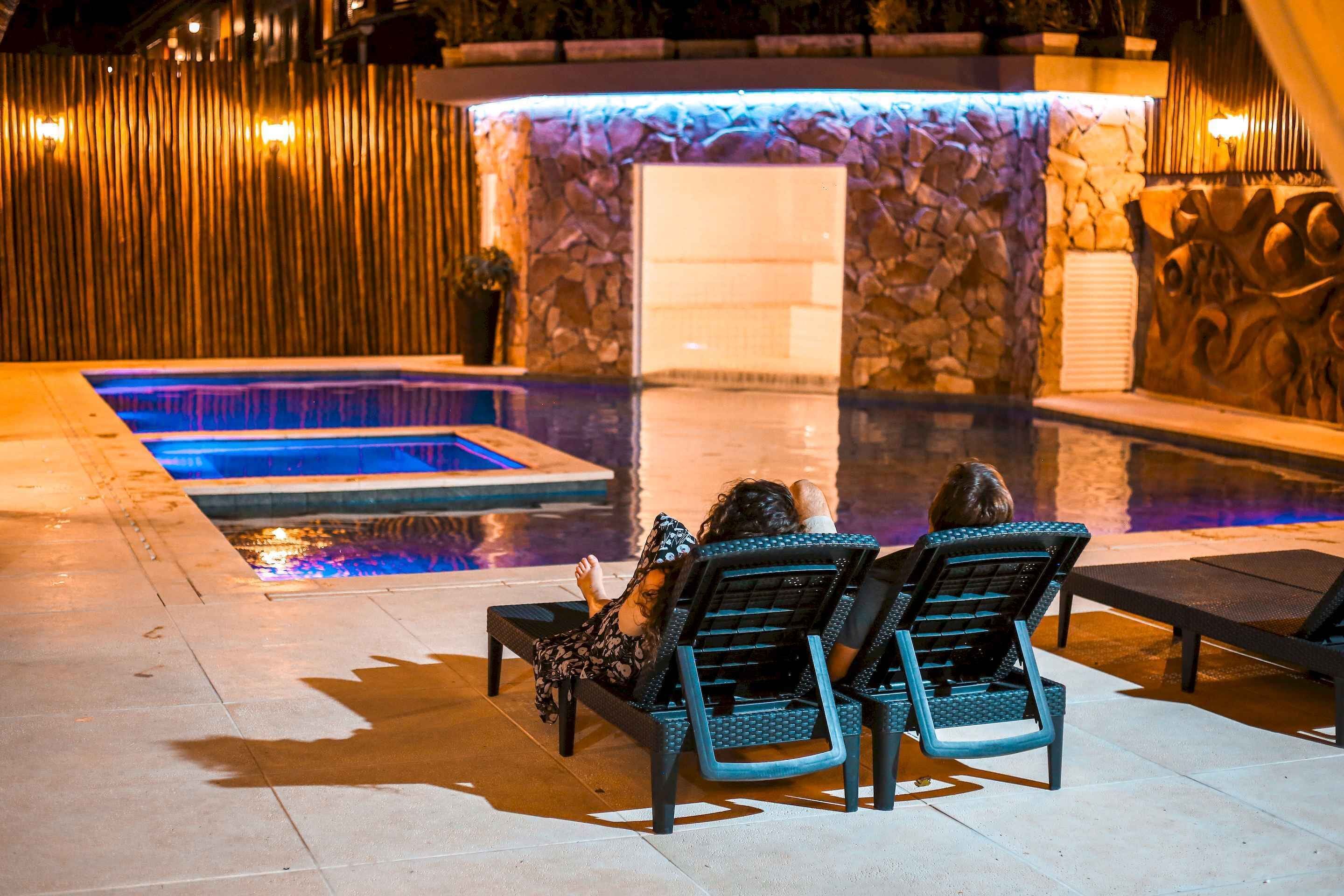 A pool area with two lounge chairs and a stone wall.