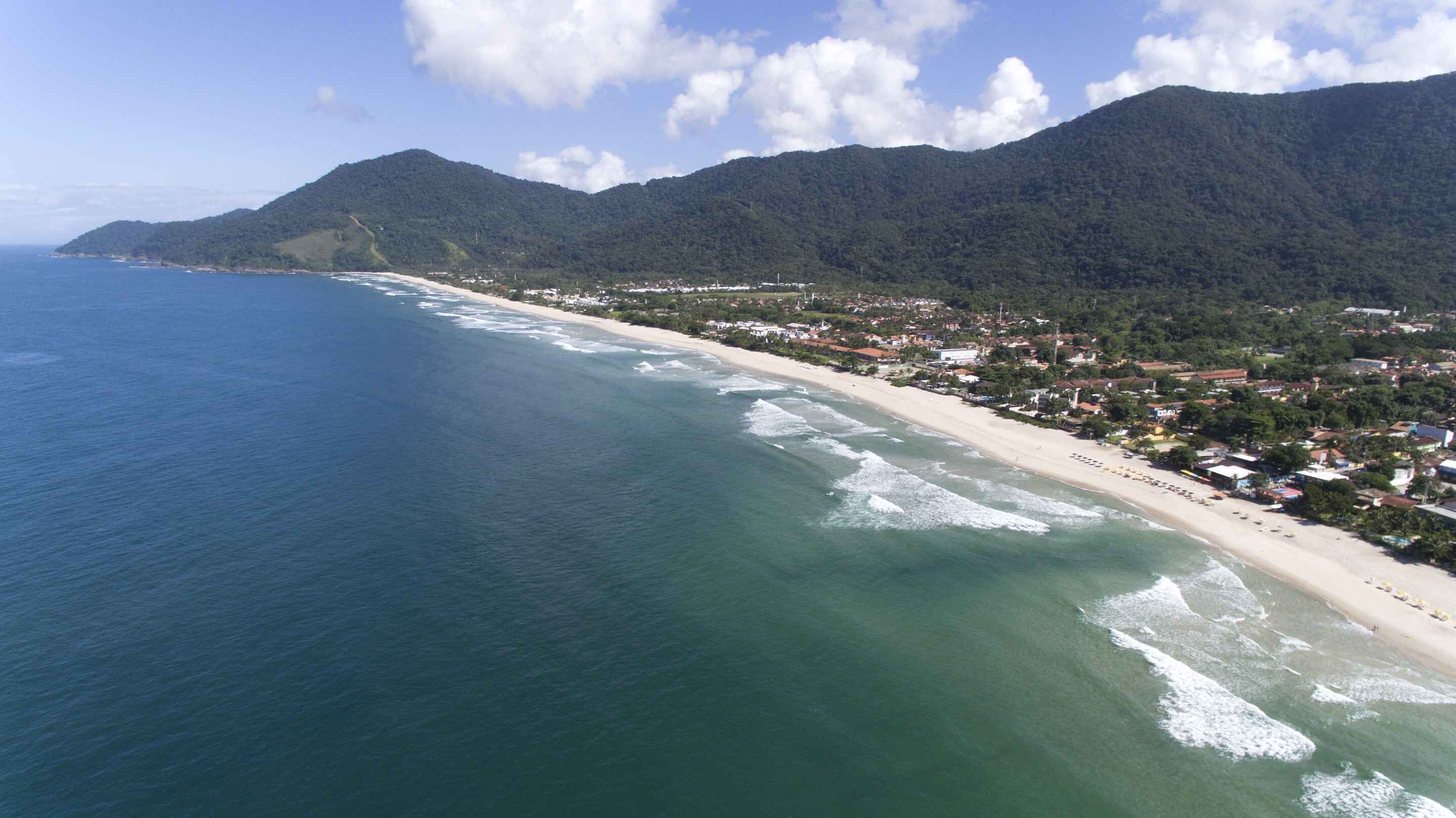 A coastal town with a beach, houses, and mountains in the background.