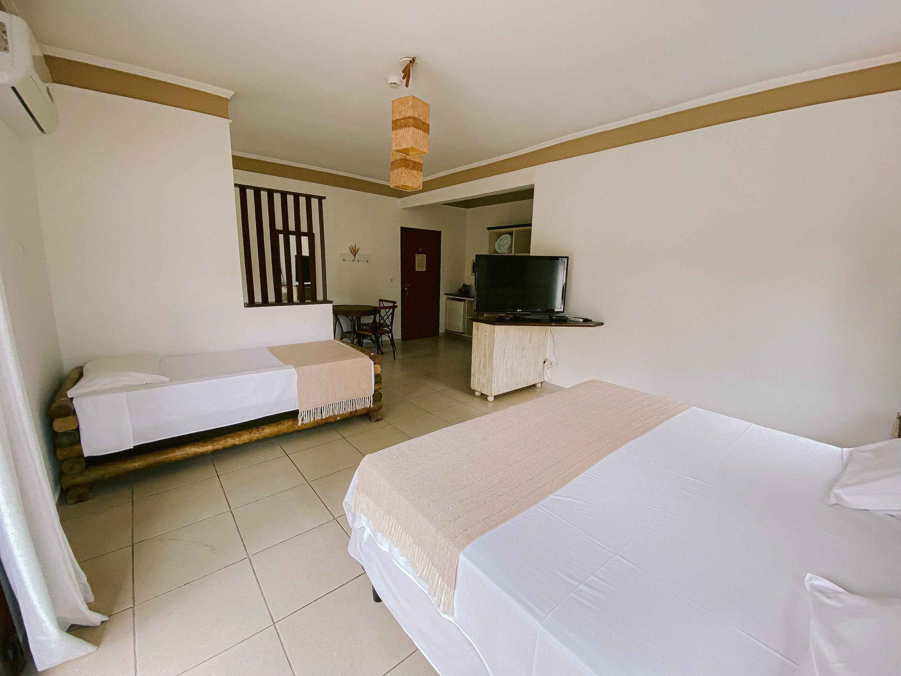 Una habitación de hotel con dos camas individuales, un televisor sobre un soporte de madera y una pequeña mesa.
