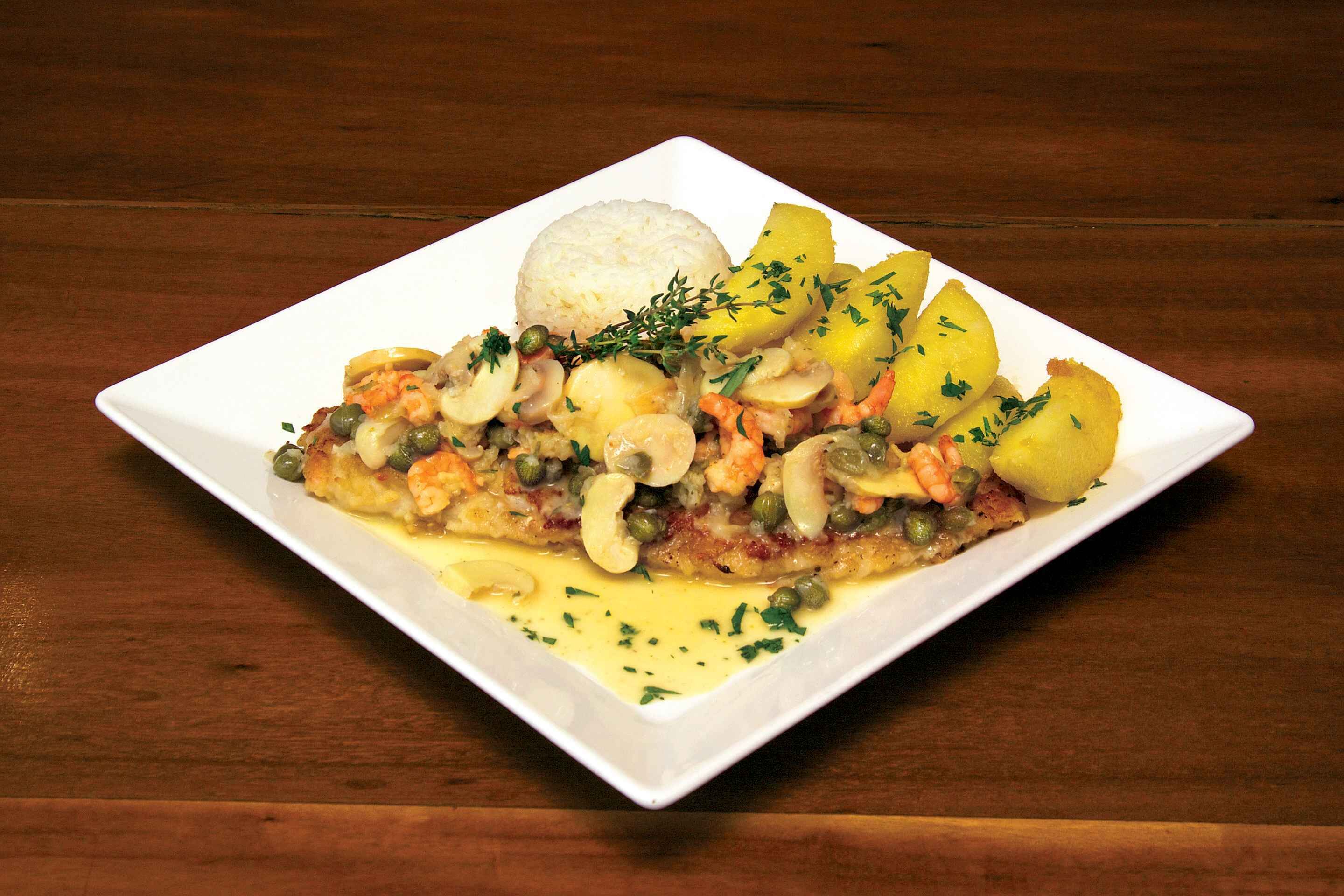 Un plato blanco y cuadrado con un plato de mariscos, papas y una porción de arroz.