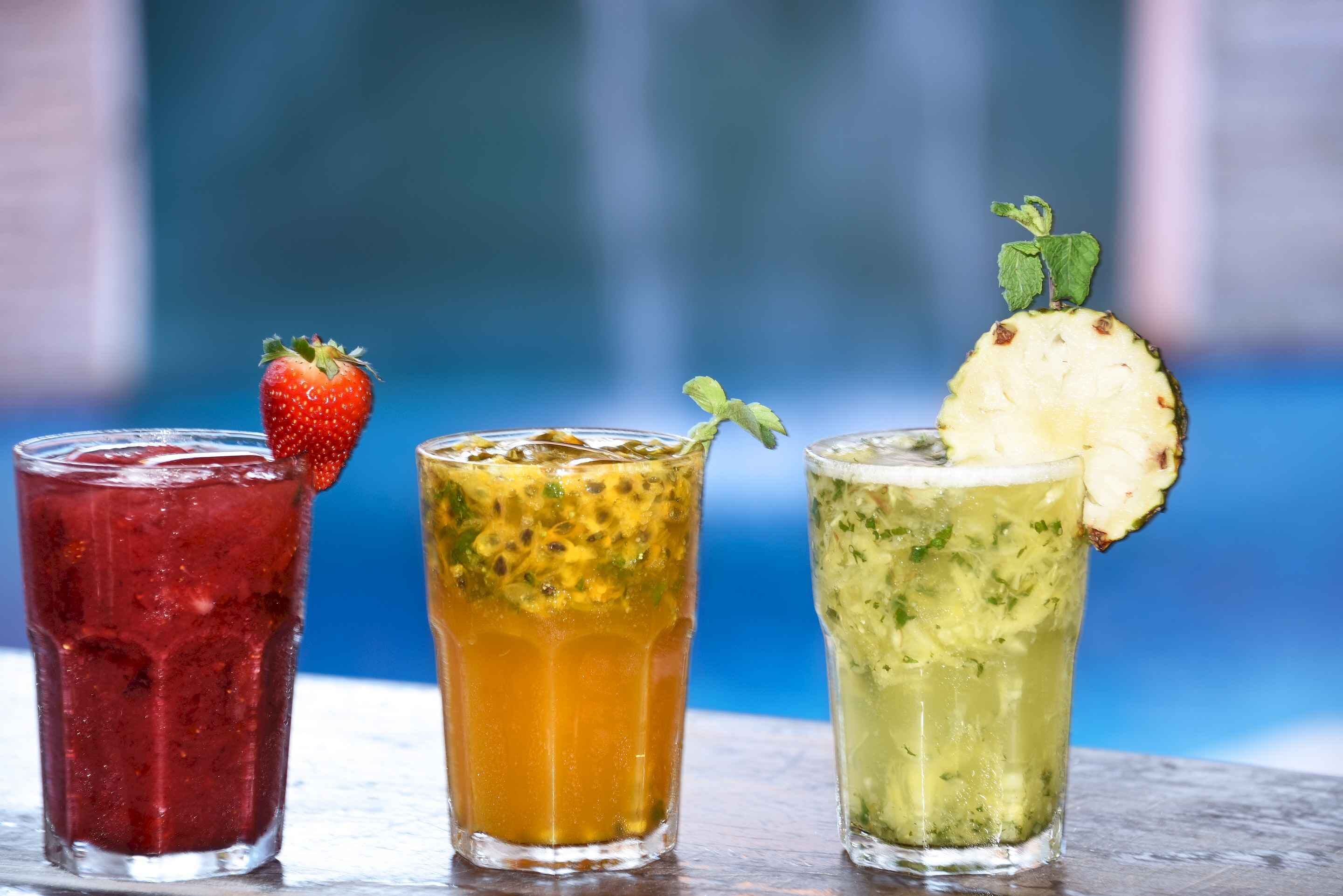 Three glasses of different colored beverages, each garnished with a fruit or herb.