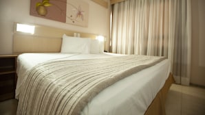 Une chambre d’hôtel avec un grand lit, une tête de lit, une œuvre d’art accrochée au mur et une fenêtre avec des rideaux.