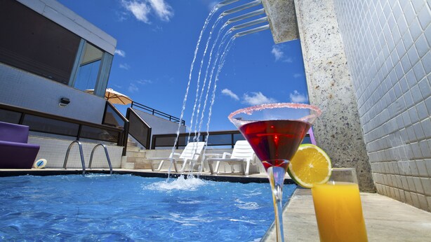Une piscine avec des jets d’eau, des chaises longues et un verre à martini garni d’une tranche d’orange.