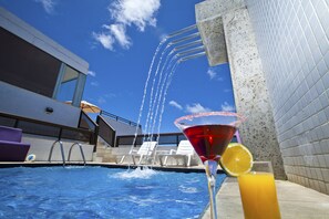 A swimming pool with water jets, lounge chairs, and a martini glass with an orange slice. - Del Canto Hotel (Aracaju)