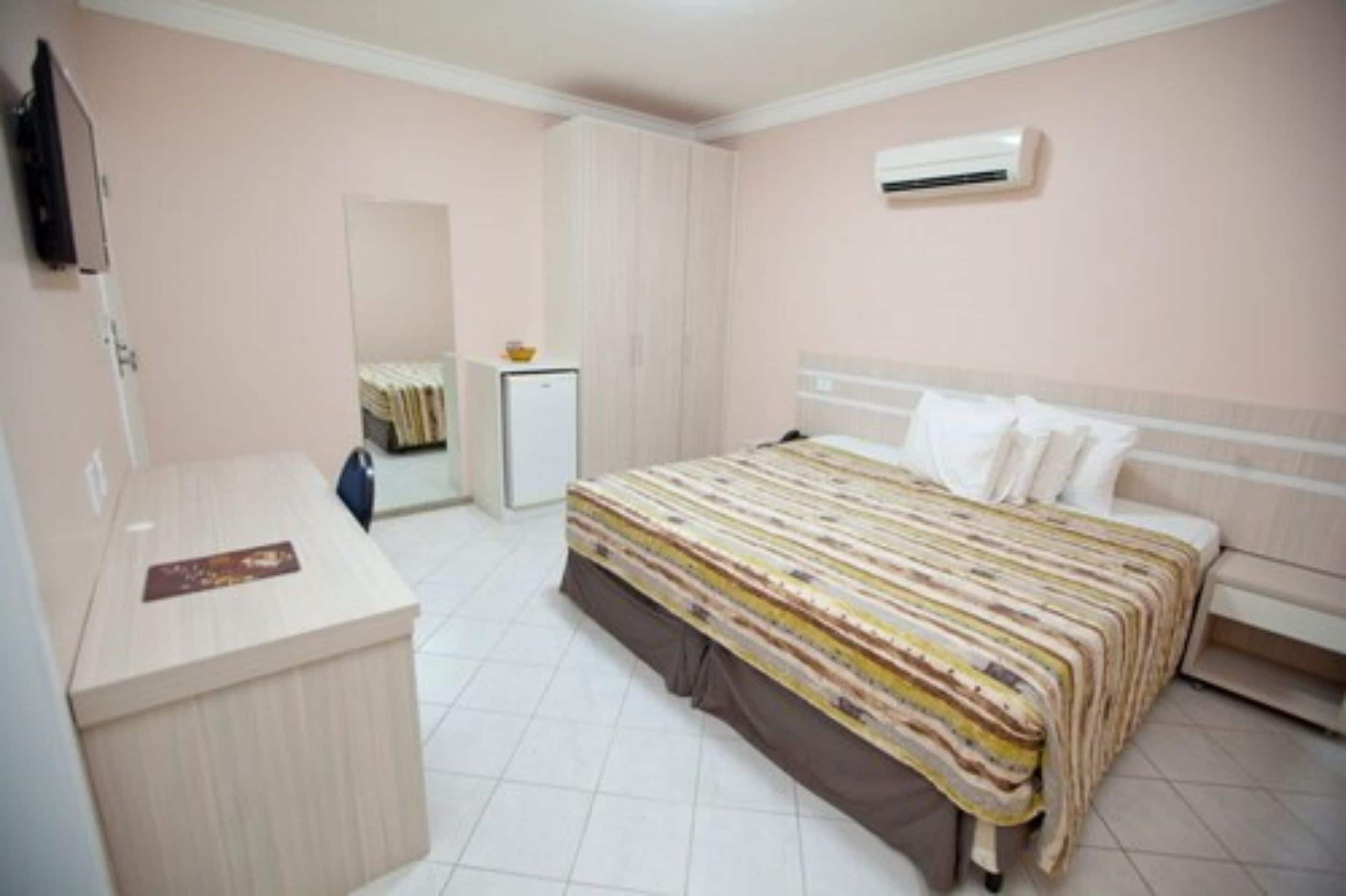 A bedroom with a bed, a desk, a wardrobe, and an air conditioner.