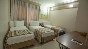 A hotel room with two single beds, a small table, and a painting on the wall.