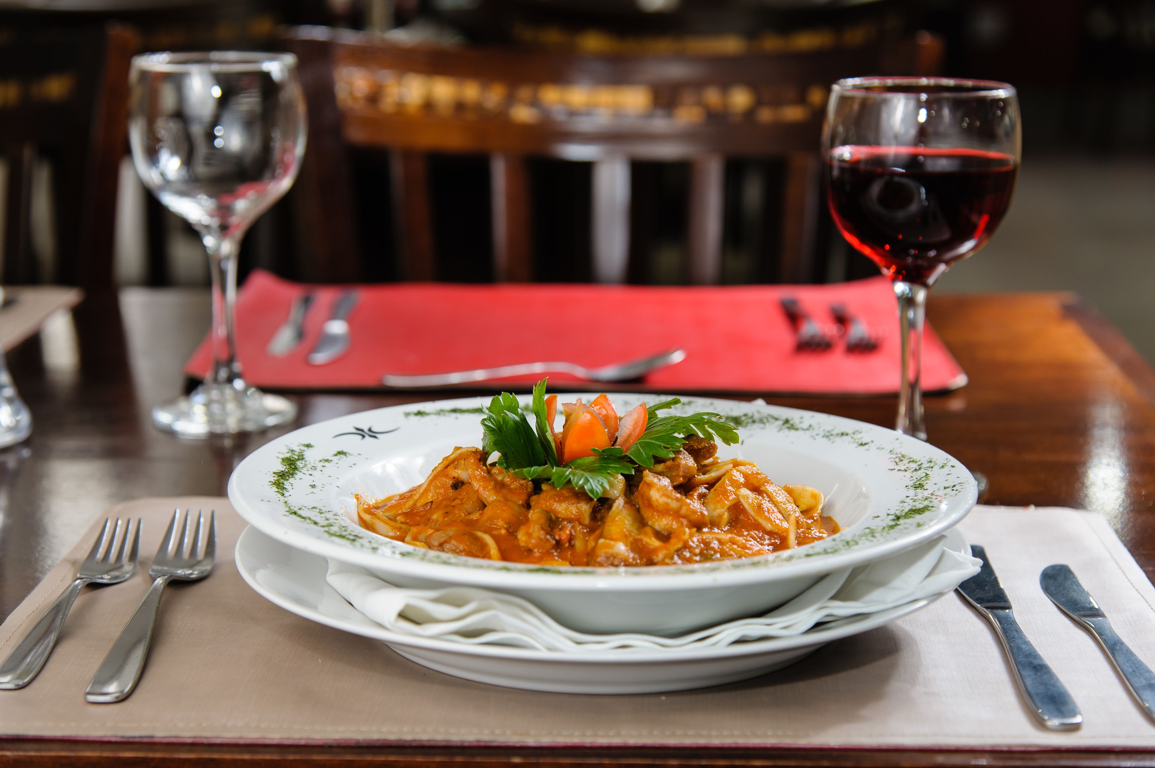 A dining table with a plate of food, cutlery, and a glass of red wine.