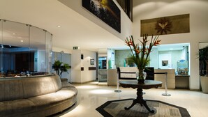 Un hall d’entrée moderne avec un canapé incurvé, une table ronde ornée d’un vase de fleurs et un comptoir d’accueil.