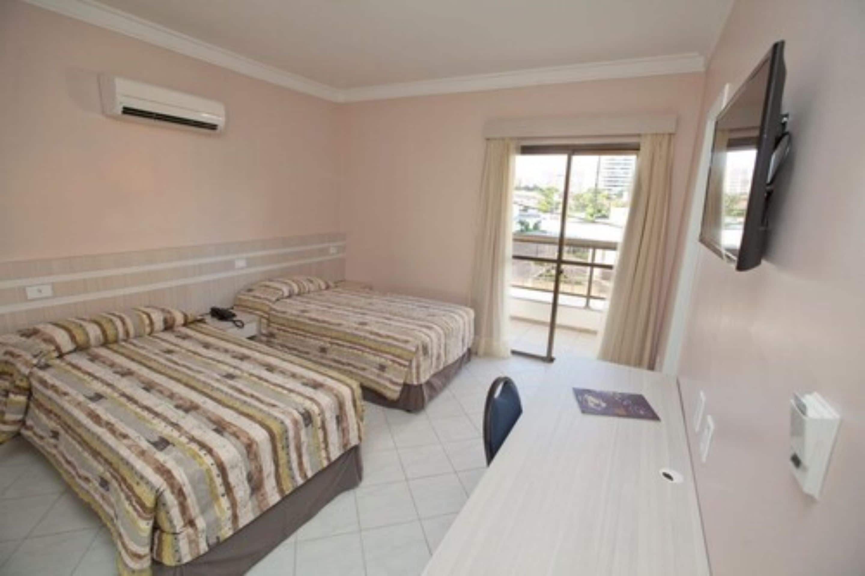 A hotel room with two beds, a TV, a desk, and a balcony with a view.