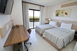 Ein Hotelzimmer mit zwei Betten, einem Schreibtisch, einem Stuhl, einem Fernseher und einem Balkon mit Aussicht.