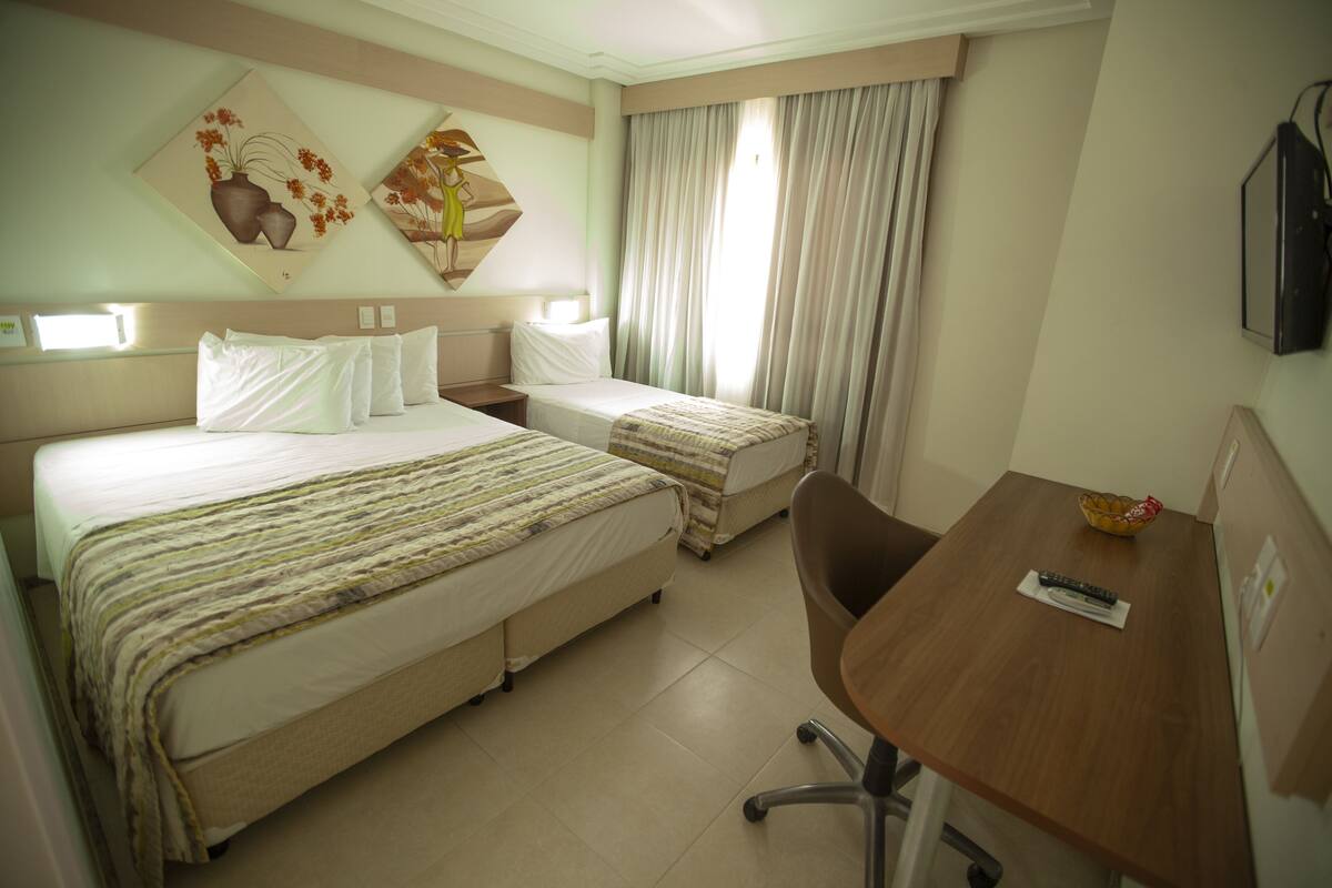 A hotel room with two beds, a desk, and a TV.