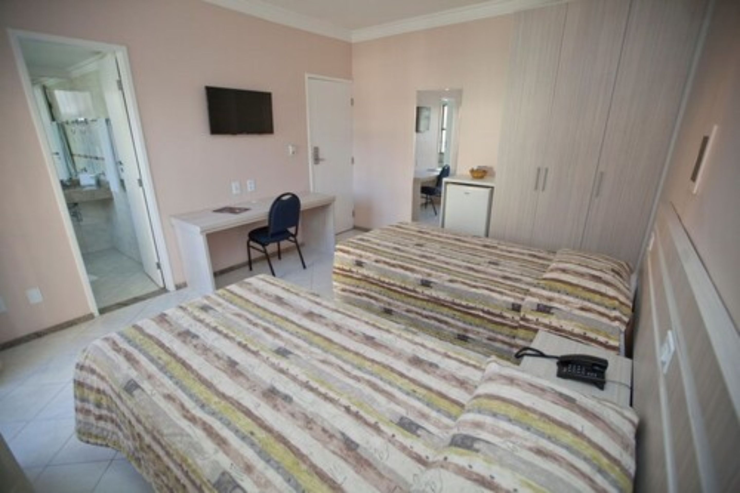 A bedroom with two beds, a desk, a chair, and a TV.