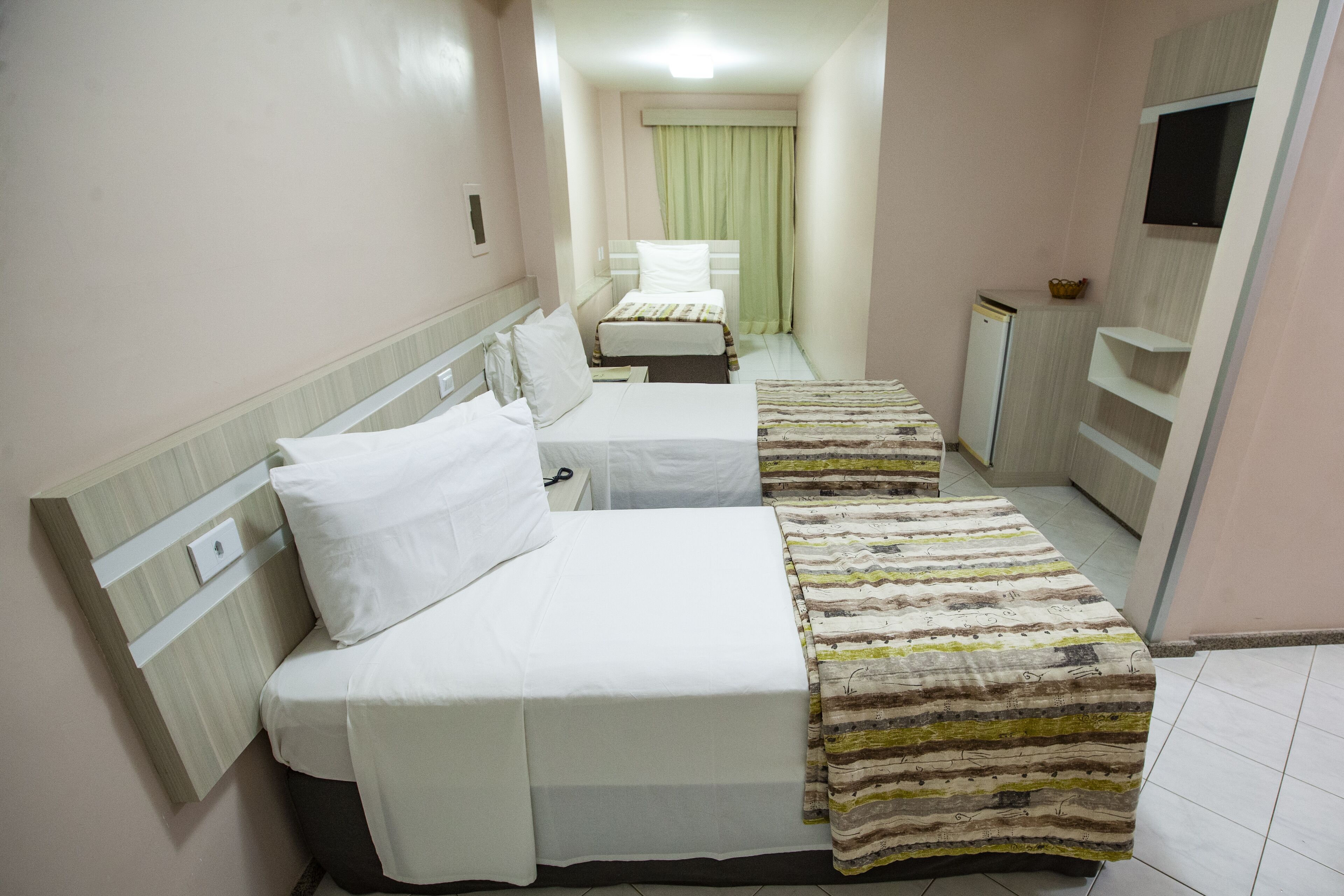Habitación de hotel con dos camas, televisión, un mueble pequeño y una ventana con cortinas.