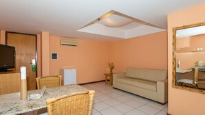 Una habitación con televisor, refrigerador pequeño, sofá, mesa de comedor con sillas y espejo.
