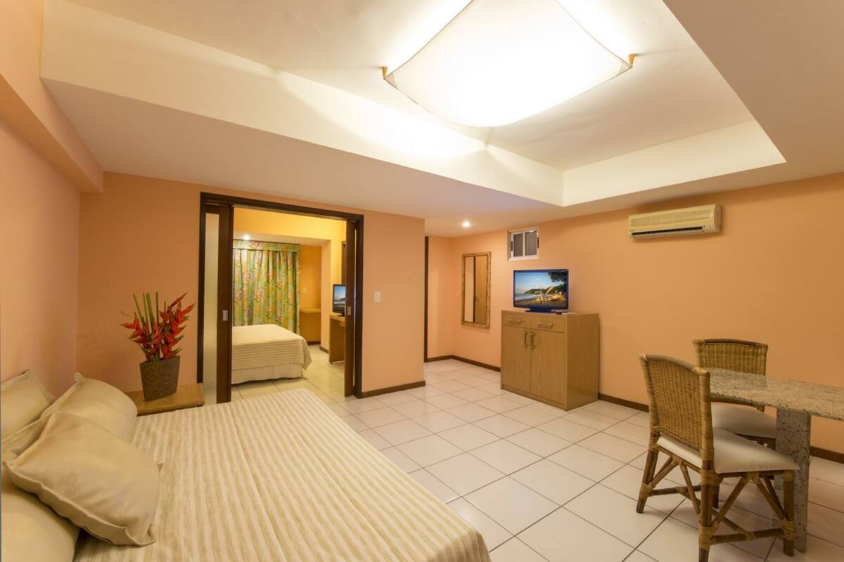 A hotel room with a bed, a desk with a chair, a television, and a small kitchenette area.