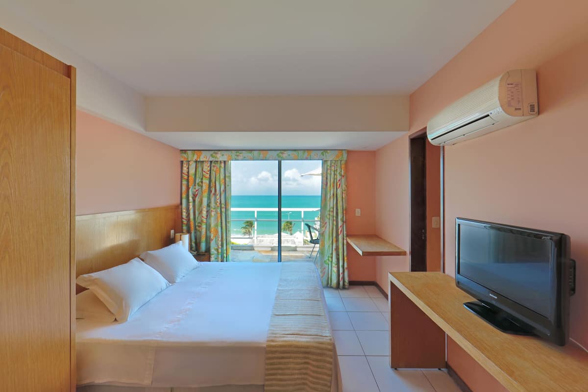 A hotel room with a bed, a television, an air conditioner, and a view of the ocean.