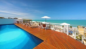 Zona junto a la piscina con sillas de descanso y sombrillas, con vista al mar azul y transparente.