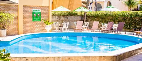 A swimming pool with lounge chairs and umbrellas, surrounded by a brick wall and greenery.