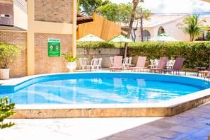 A swimming pool with lounge chairs and umbrellas, surrounded by a brick wall and greenery. - Pizzato Praia Hotel (Natal)