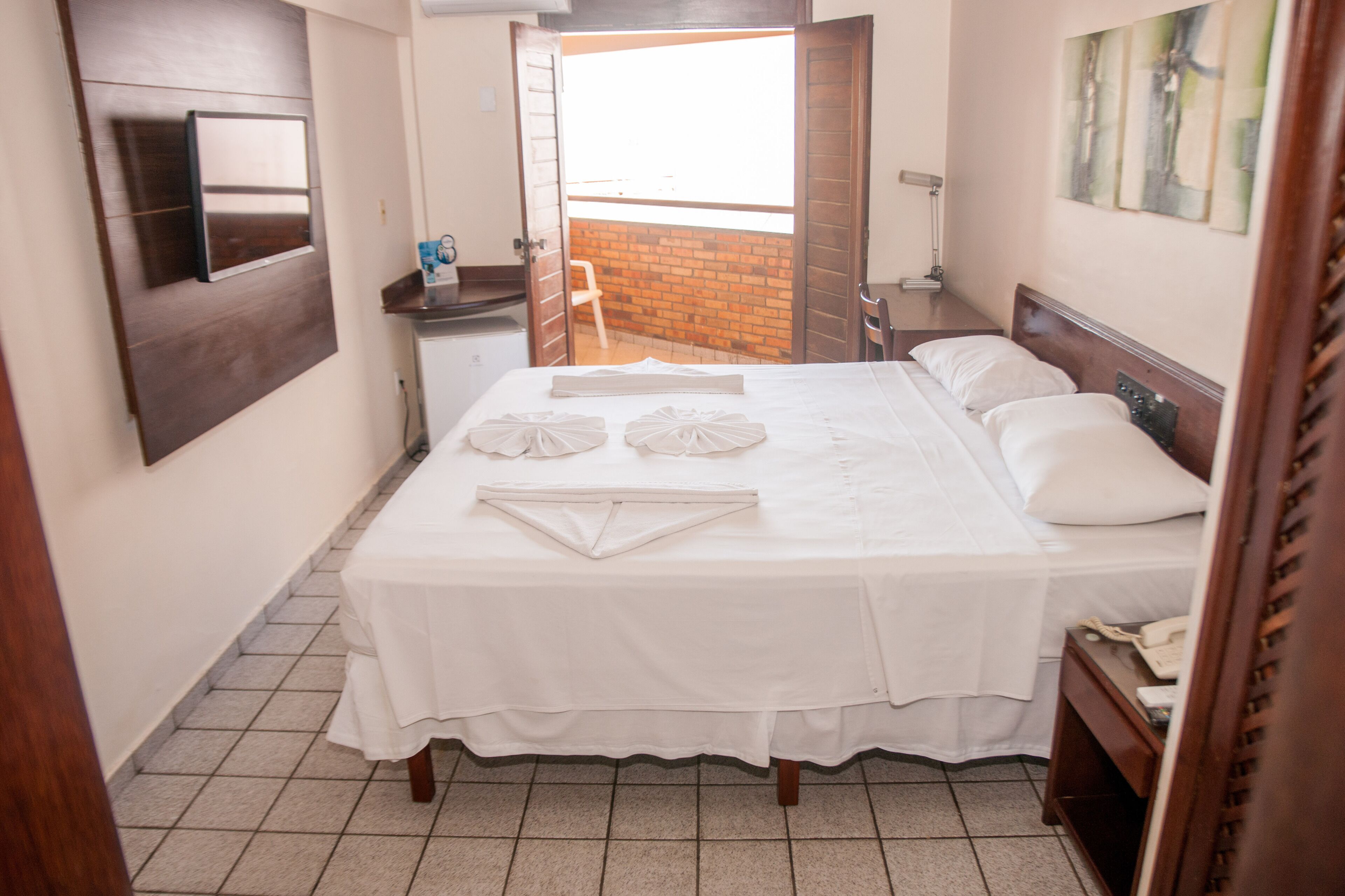 A hotel room with a bed, a desk, a chair, and a view of the outside.