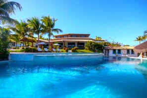 A swimming pool with lounge chairs and palm trees, surrounded by a building with a tiled roof. - Hotel Tibau Lagoa (Tibau do Sul)