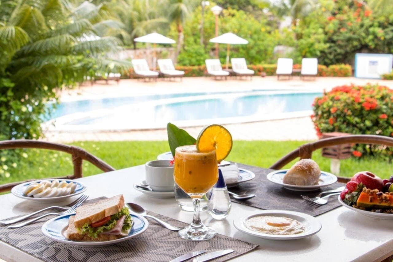 Una mesa de comedor con comida, un vaso de jugo de naranja y vista a una piscina.