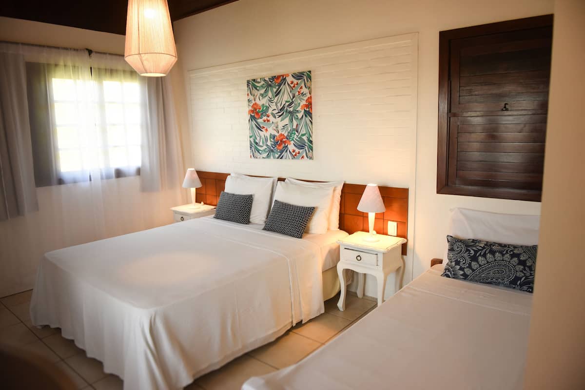 A bedroom with a large bed, two bedside tables, a hanging light fixture, a window with curtains, and a wall-mounted artwork.