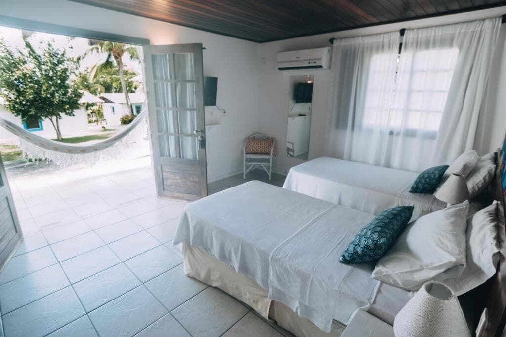 A room with two beds, a hammock, a chair, and a view of the outside.