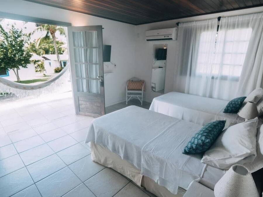 A room with two beds, a hammock, a chair, and a view of the outside.