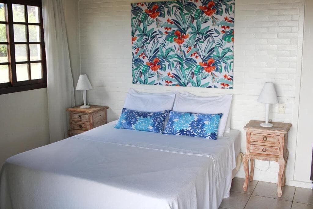 Un dormitorio con cama, dos mesitas de noche, una ventana y un tapiz con motivos florales.