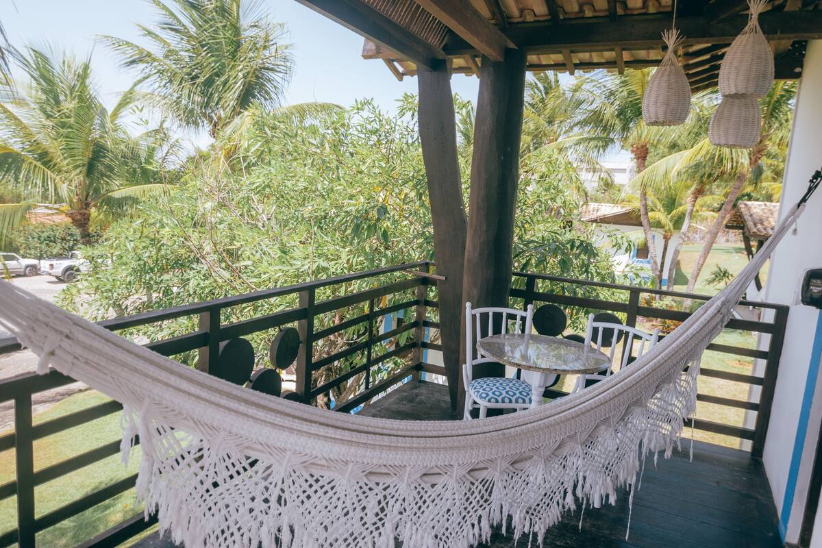 A hammock chair on a wooden deck with a view of palm trees and a car in the background.